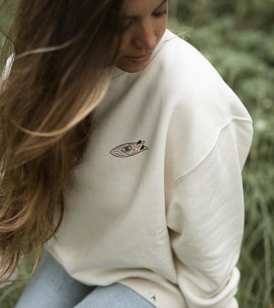 woman wearing organic cotton crewneck with fish eye surfboard design on the front