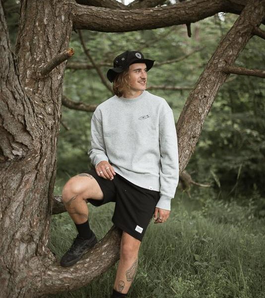 Young man sitting on a tree branch wearing collab of Hands For Feet and INMIND Clothing Grey crewneck