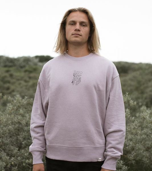 model standing tall with lilac purple crewneck in front of green field