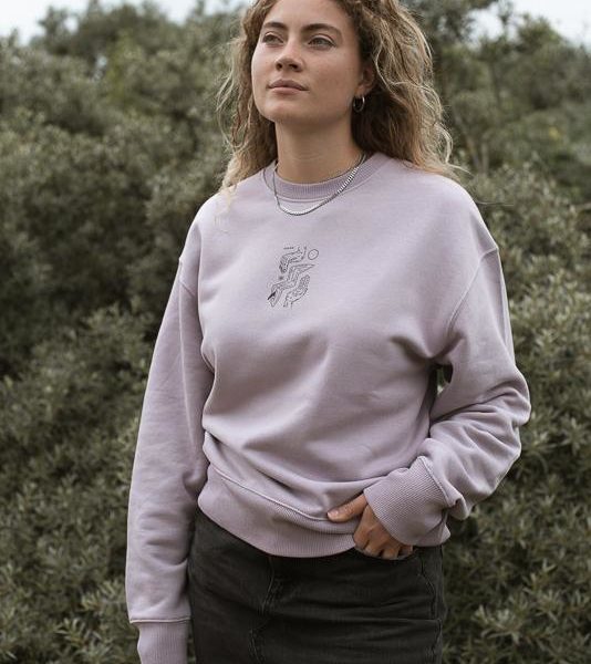 woman posing in grass of green field with lilac petal crewneck
